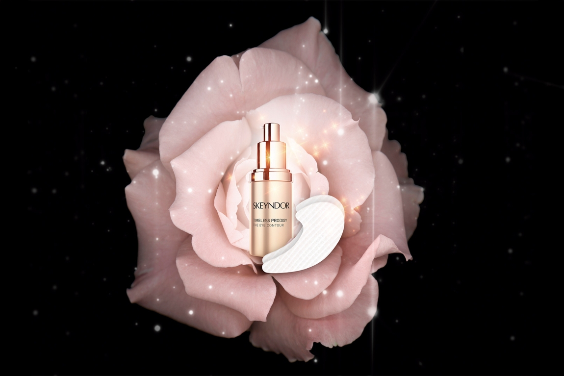 Flakon mit Aufschrift 'SKEYNDOR' und Kosmetikpad vor einer großen, geöffneten Blüte auf schwarzem Hintergrund